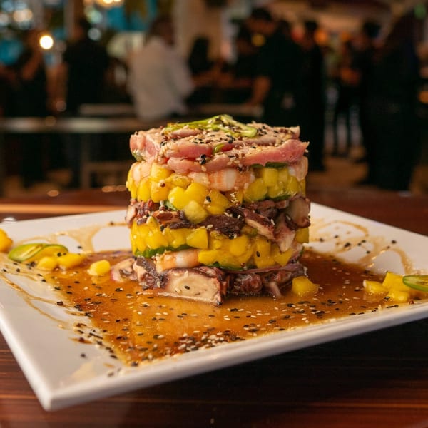 Stacked seafood tower with tuna, shrimp, octopus, mango, and jalapeños, drizzled with sauce.