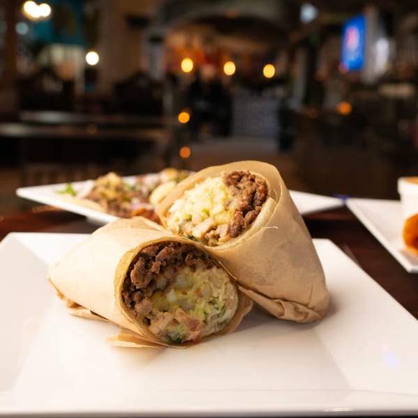 Two large burritos, wrapped in paper, filled with meat and rice, on a white plate.