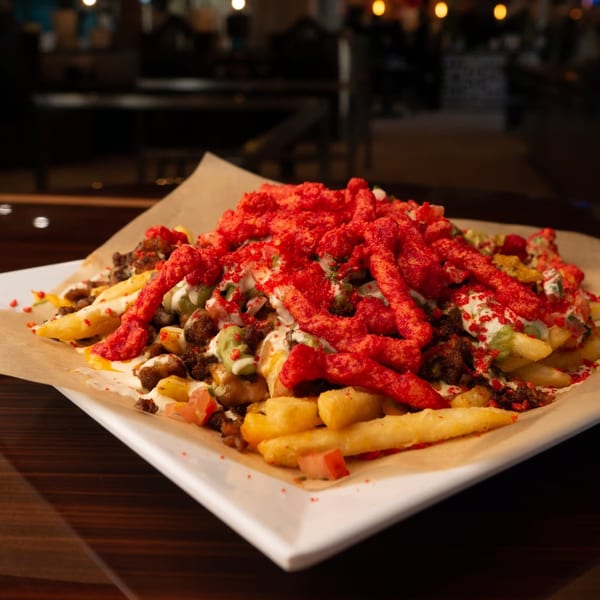 Loaded fries topped with red hot crunchy snacks, meat, guacamole, and sour cream.